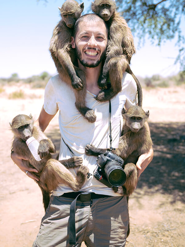 namibia-man-with-camera-holding-four-baby-baboons-YKXWTT5f